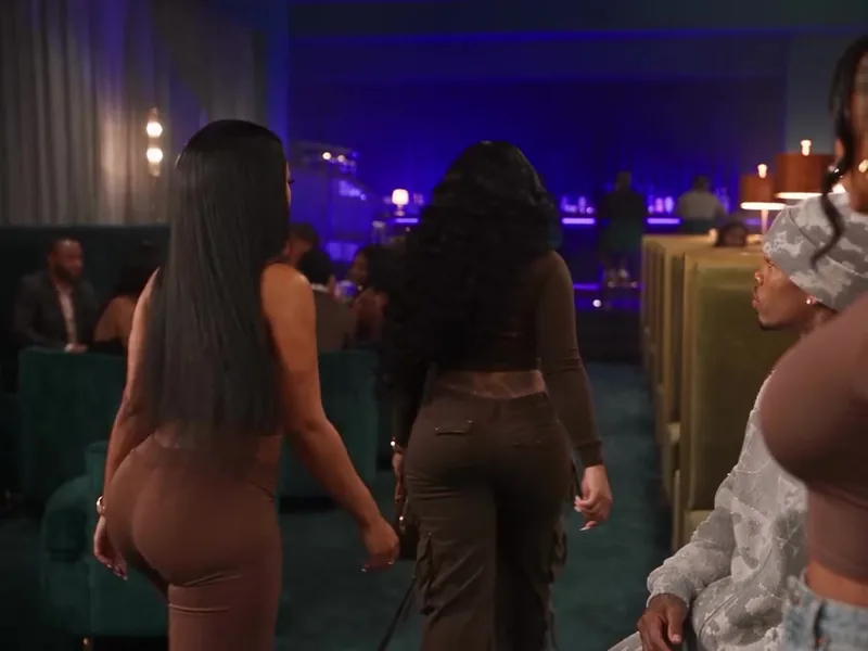 Two women in brown walk away through the purple-lit lounge